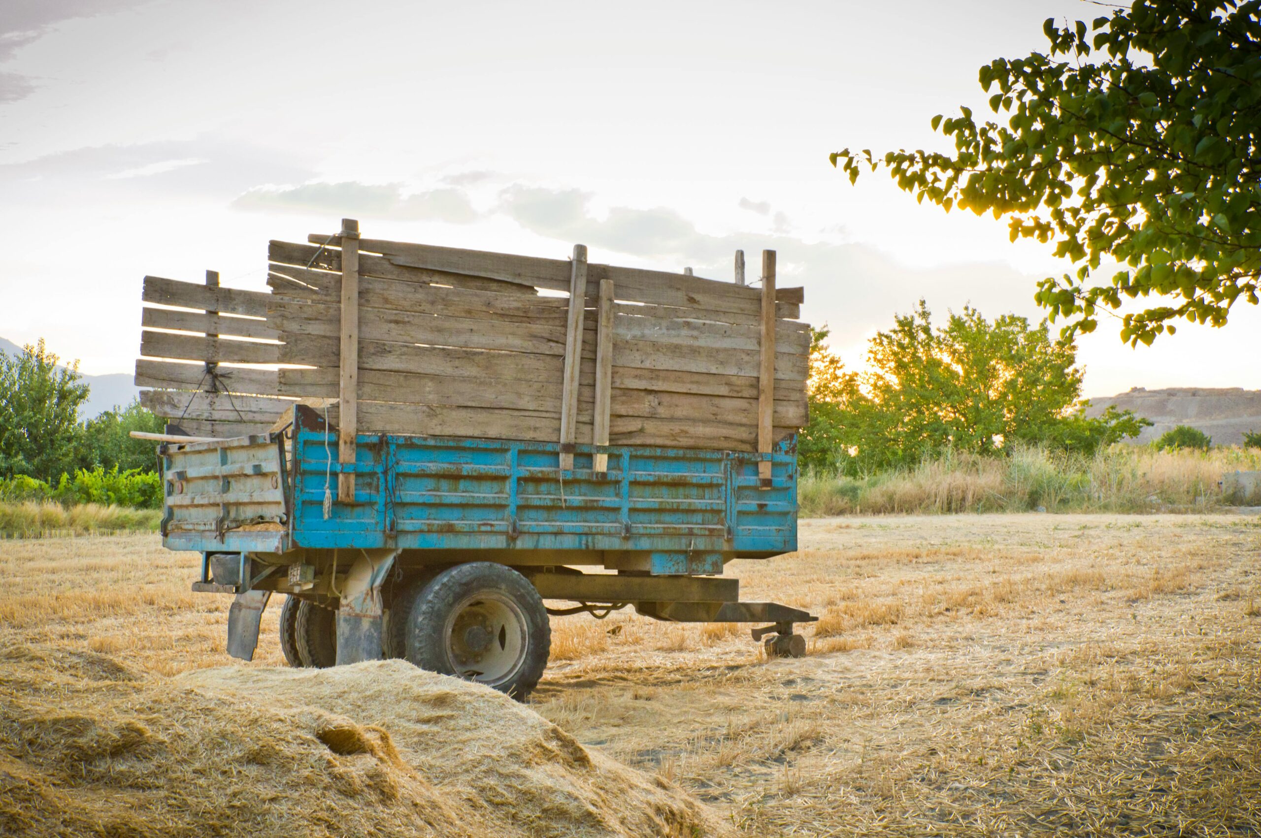 A wooden farm trailer on a rural hay field at sunset, symbolizing agriculture.